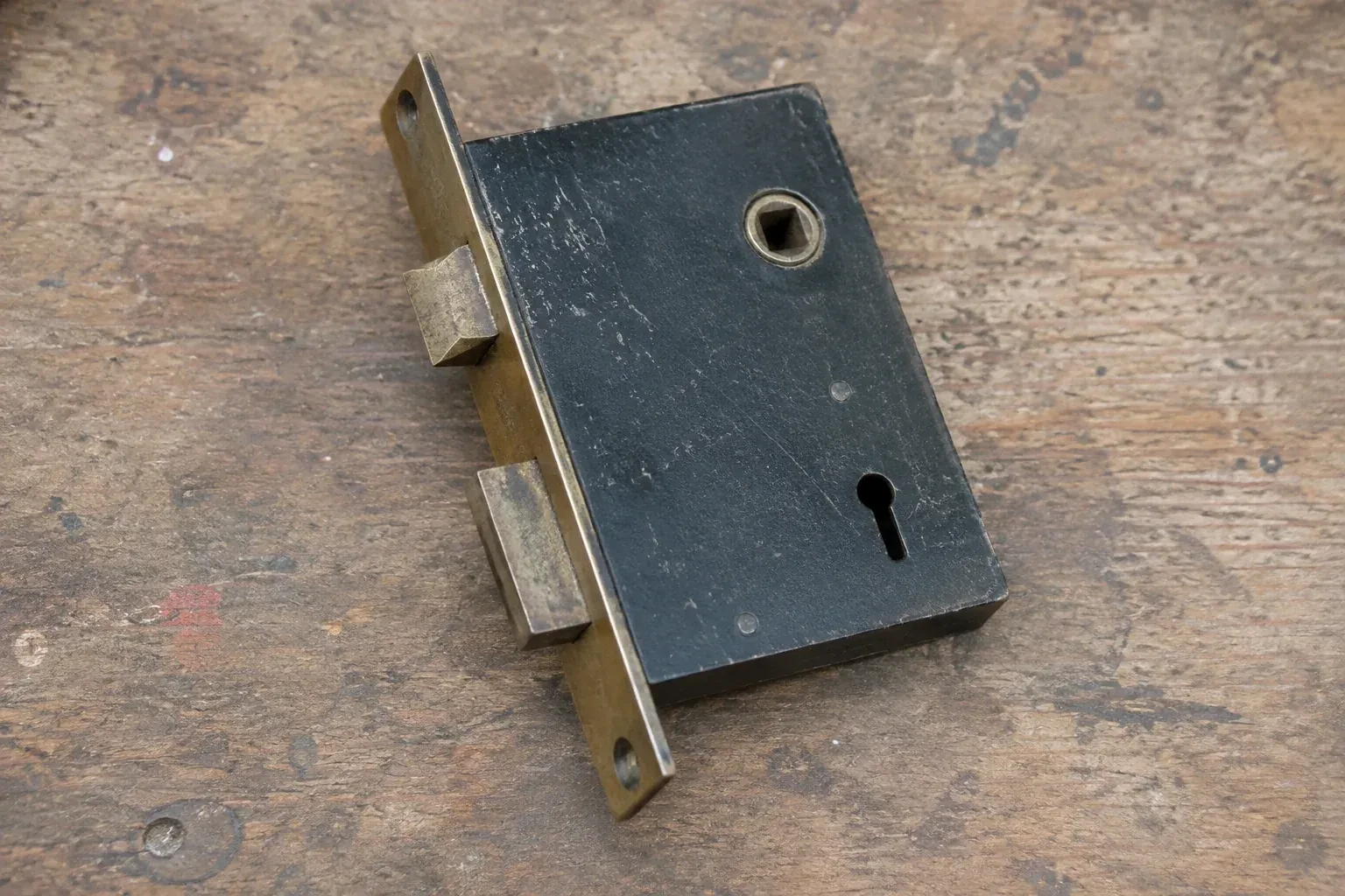 Closed mortise lock case with spindle opening, keyhole, latch and deadbolt on a wooden workbench. — Vintage Mortise Lock Service, Vaughan