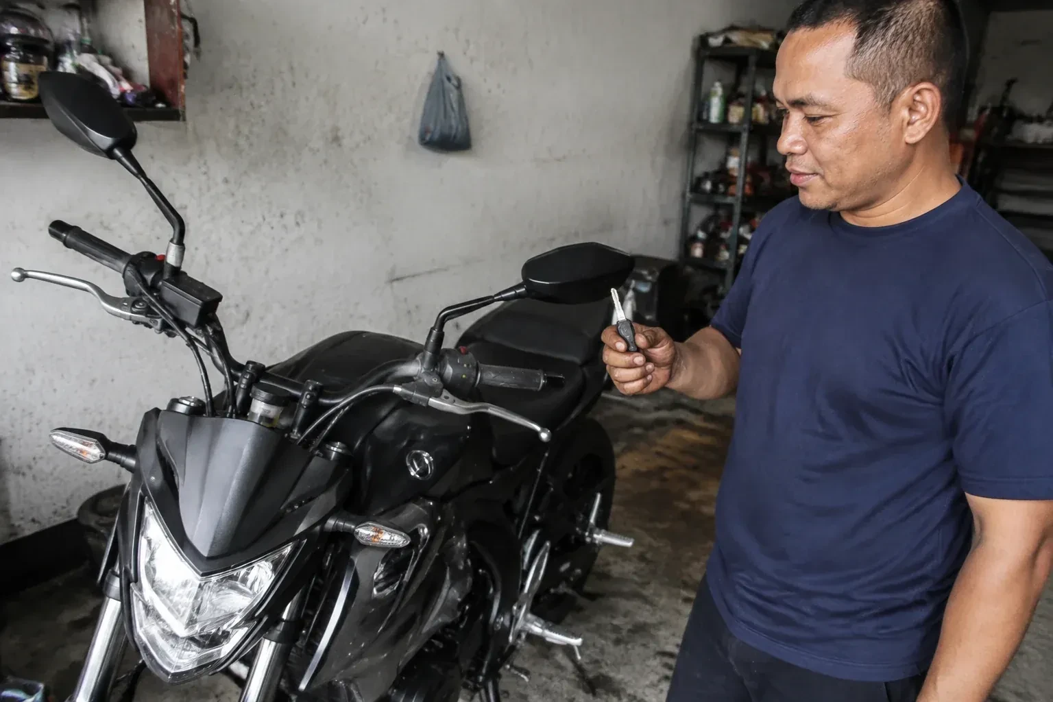 Person holding a key beside a black motorcycle in a garage. — Motorcycle & Scooter Keys, Vaughan